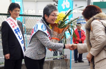 花束を手にし握手する氏平県議候補。そのうしろは林市議。